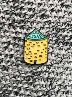 A small pin in the shape of a round prehistoric stone structure (yellow with a green roof)