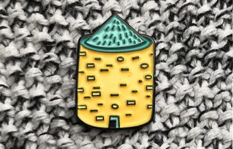 A small pin in the shape of a round prehistoric stone structure (yellow with a green roof)