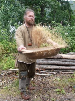 A man in prehistoric costume throwing barley from a bowl into the air
