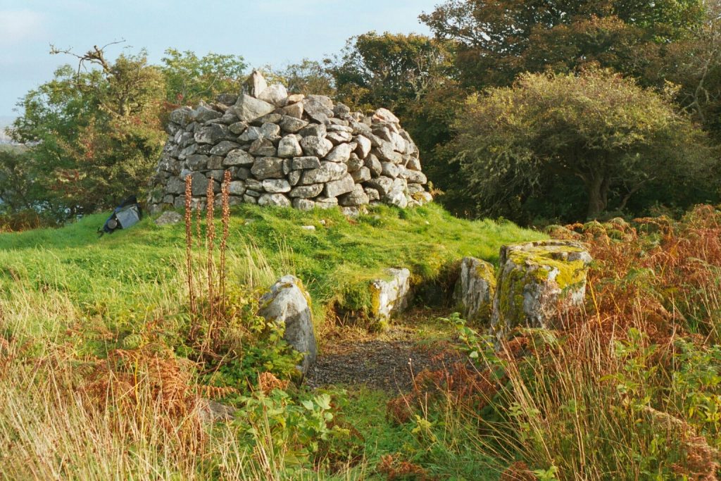 Photo of a large stone mound in a field, with smaller stones in front.
