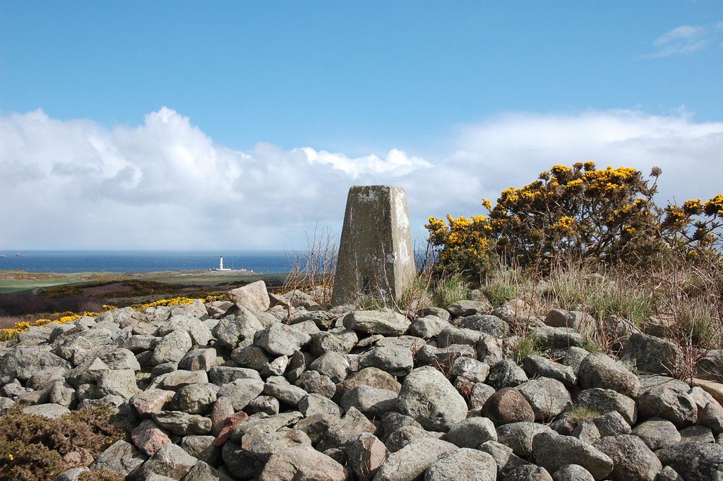 Photo of a pile of large stones atop a low hill with a trig marker at the top.