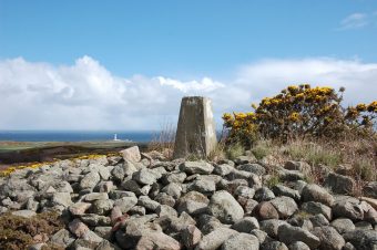 Photo of a pile of large stones atop a low hill with a trig marker at the top.