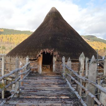 Photo of a wooden water dwelling at the end of a wooden walkway, with a pointed roof.