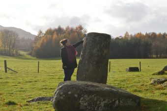 Photo of a woman placing a hand on a large standing stone in a field.