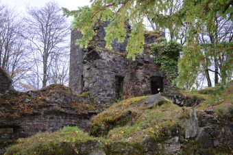 Photo of the ruins of a dark stone castle covered in moss and lychen.
