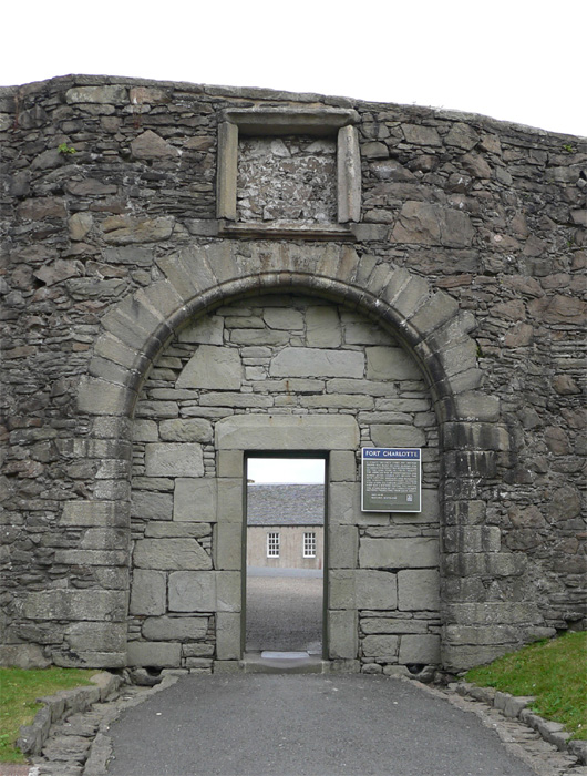 Photo of a tall grey stone archway with a small rectangular doorway cut into it.