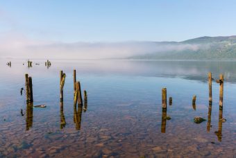 Photo of the edge of a loch with mist rolling over it in the distance.