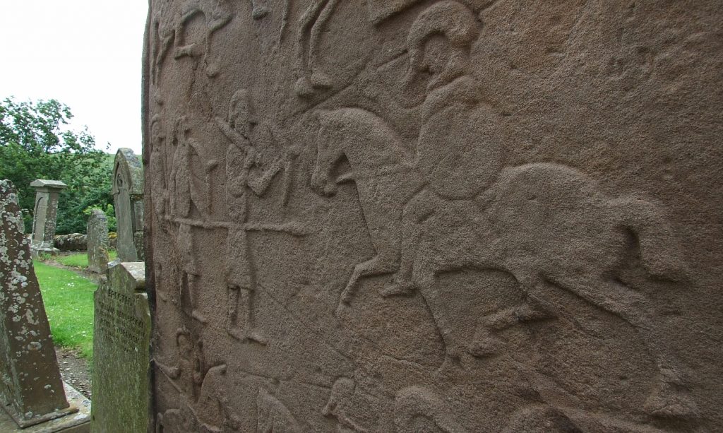 Photo of a carved standing stone with soldiers and horses.