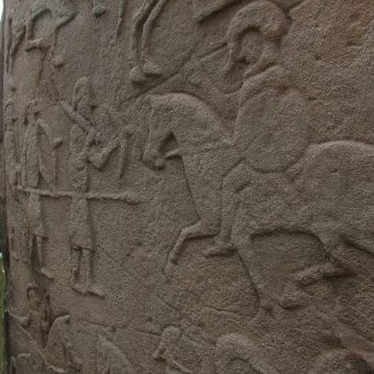 Photo of a carved standing stone with soldiers and horses.