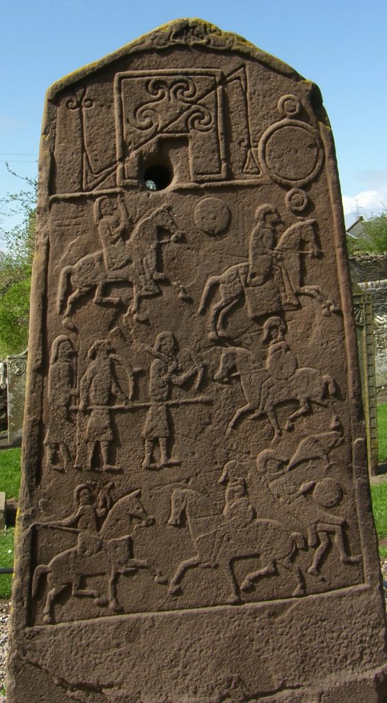 Photo of a large standing stone slab with cravings depicting soldiers and men on horseback engaged in battle.