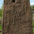 Photo of a large standing stone slab with cravings depicting soldiers and men on horseback engaged in battle.