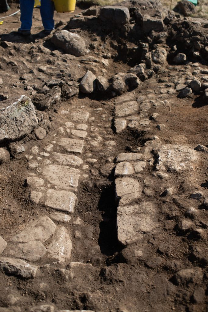 Photo of the foundations of a stone wall at the bottom of an archaeological trench.