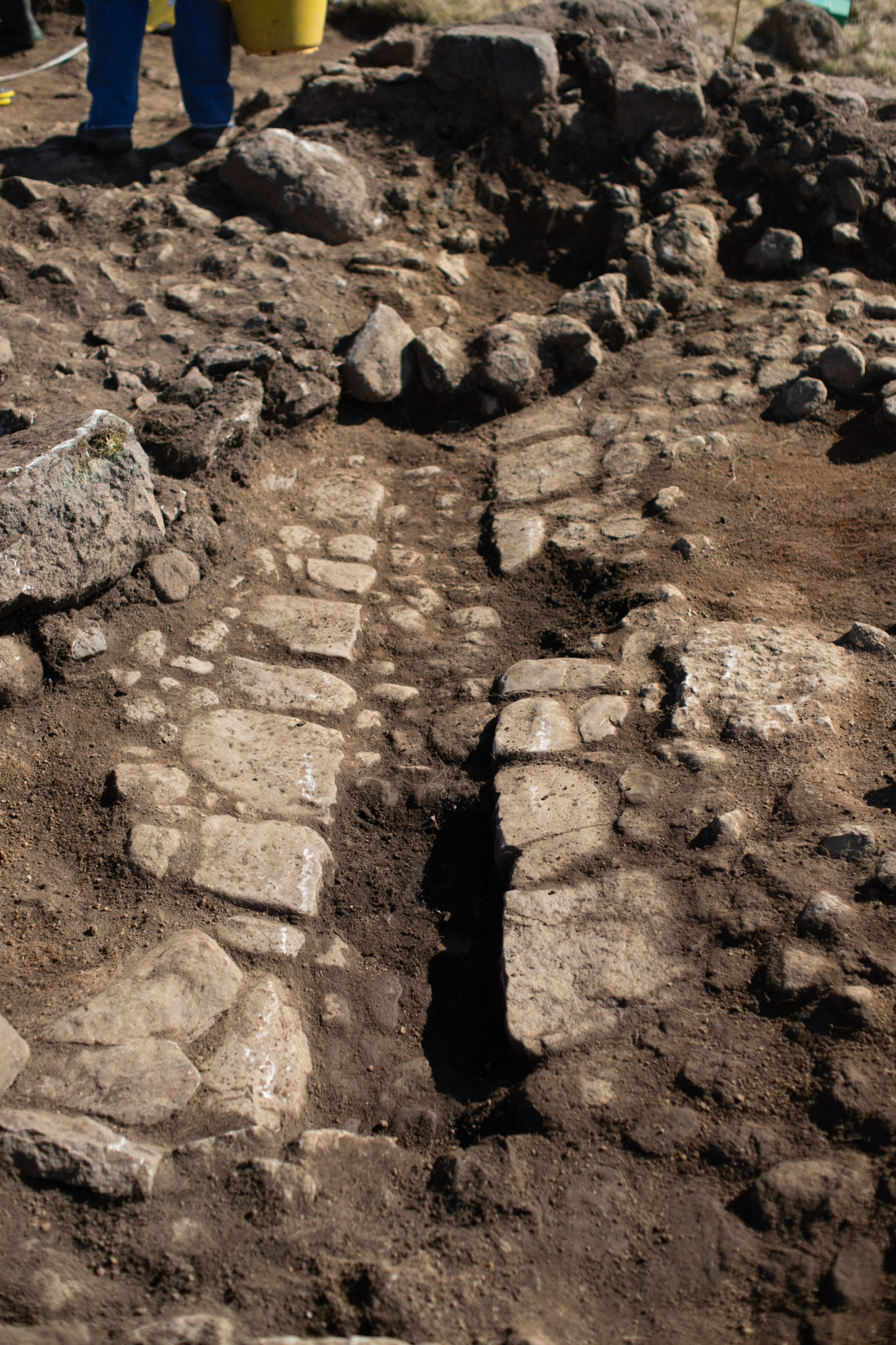 Photo of the foundations of a stone wall at the bottom of an archaeological trench.