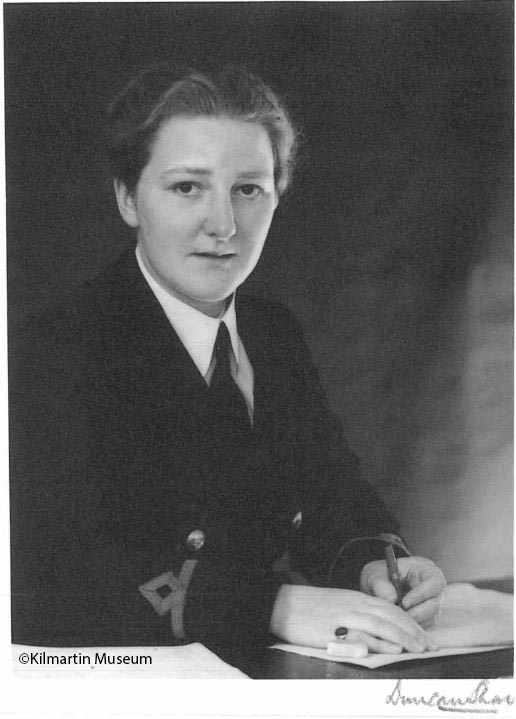 Black and white portrait of a young woman in military uniform sat at a desk.