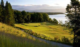 Photo of a golf course by a loch in the evening sun.