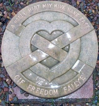 Photo of a stone memorial placque on the ground with a heart and two crosses running through it.