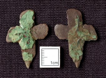 Photo of two corroded cross-shaped pendants.