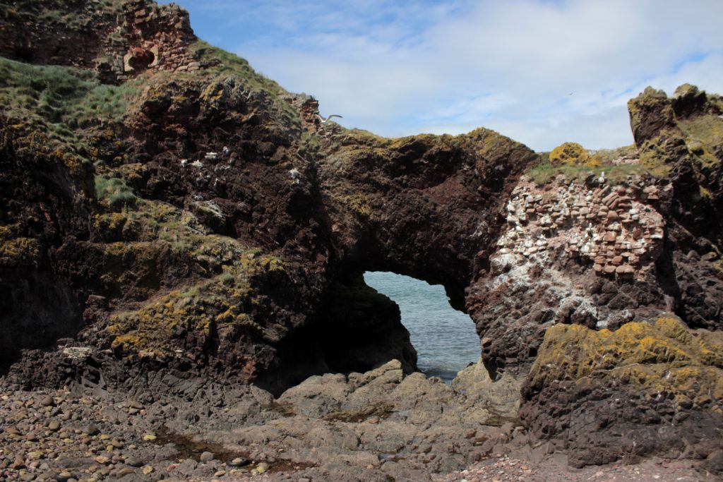 Photo of a decaying low archway cut into rock and supported by red brick.