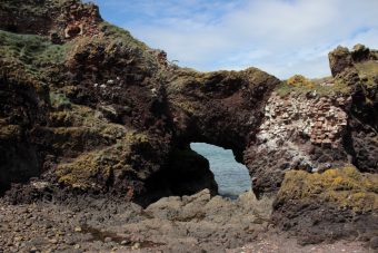 Photo of a decaying low archway cut into rock and supported by red brick.