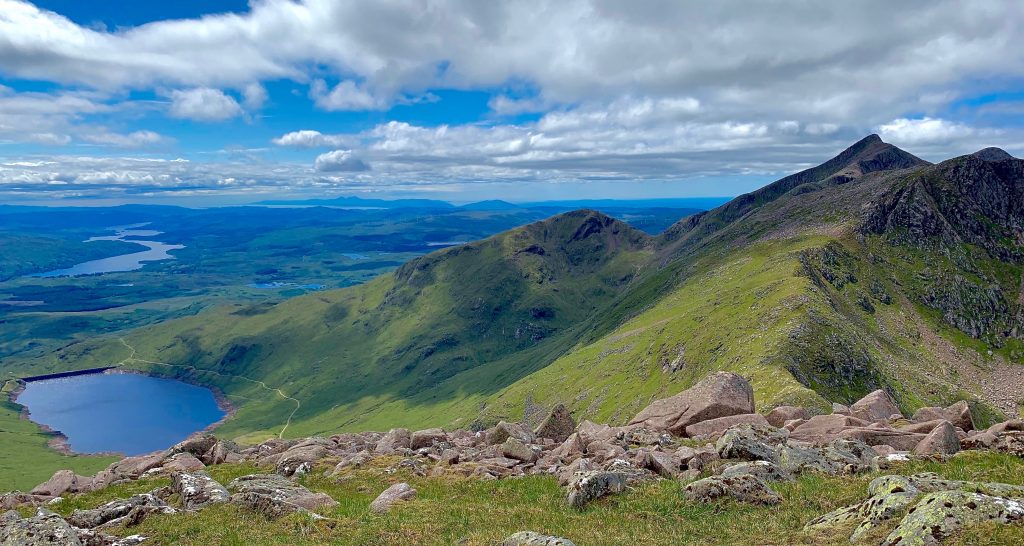 Photo of a panoramic view of a mountain range with a loch at the bottom.