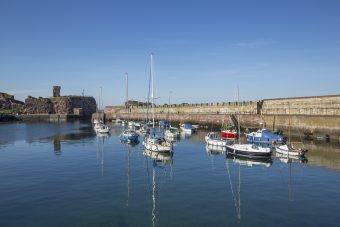 Photo of a small harbour on a clear day, with a ruined castle in the background.