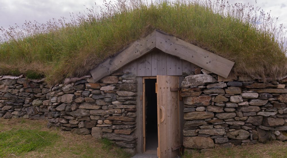 Photo of a Viking longhouse reconstruction, with an arched lintel above the door and a turf roof