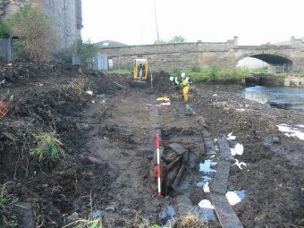 Wooden boat buried in the mud with someone in a high vis jacket in the background