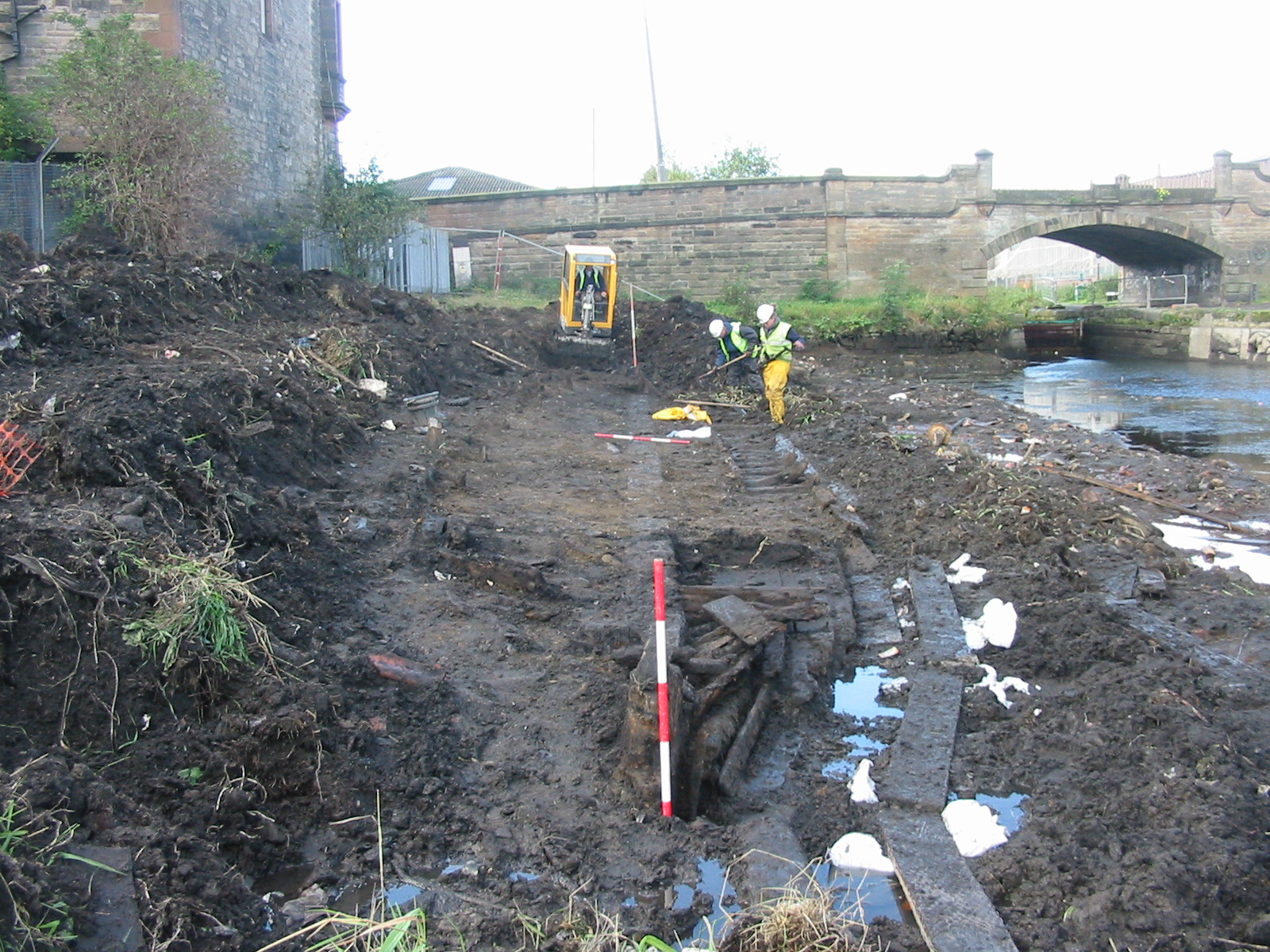 Wooden boat buried in the mud with someone in a high vis jacket in the background