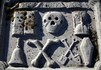 Grave slab with book, skull, hourglass, bell, bones, tools and a coffin