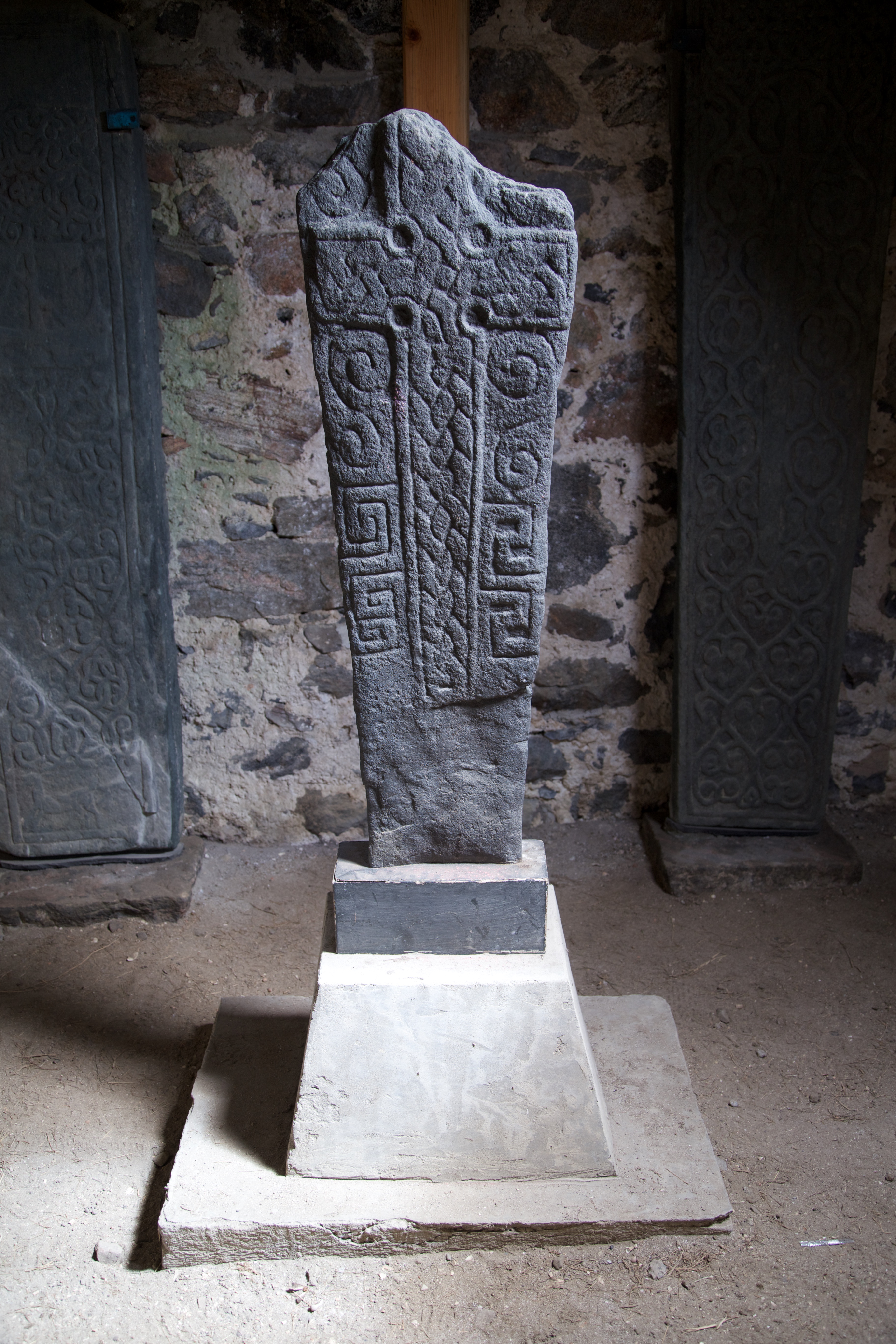 Photo of a grey carved stone sculpture, on a plinth, with a carved Celtic cross on the front.