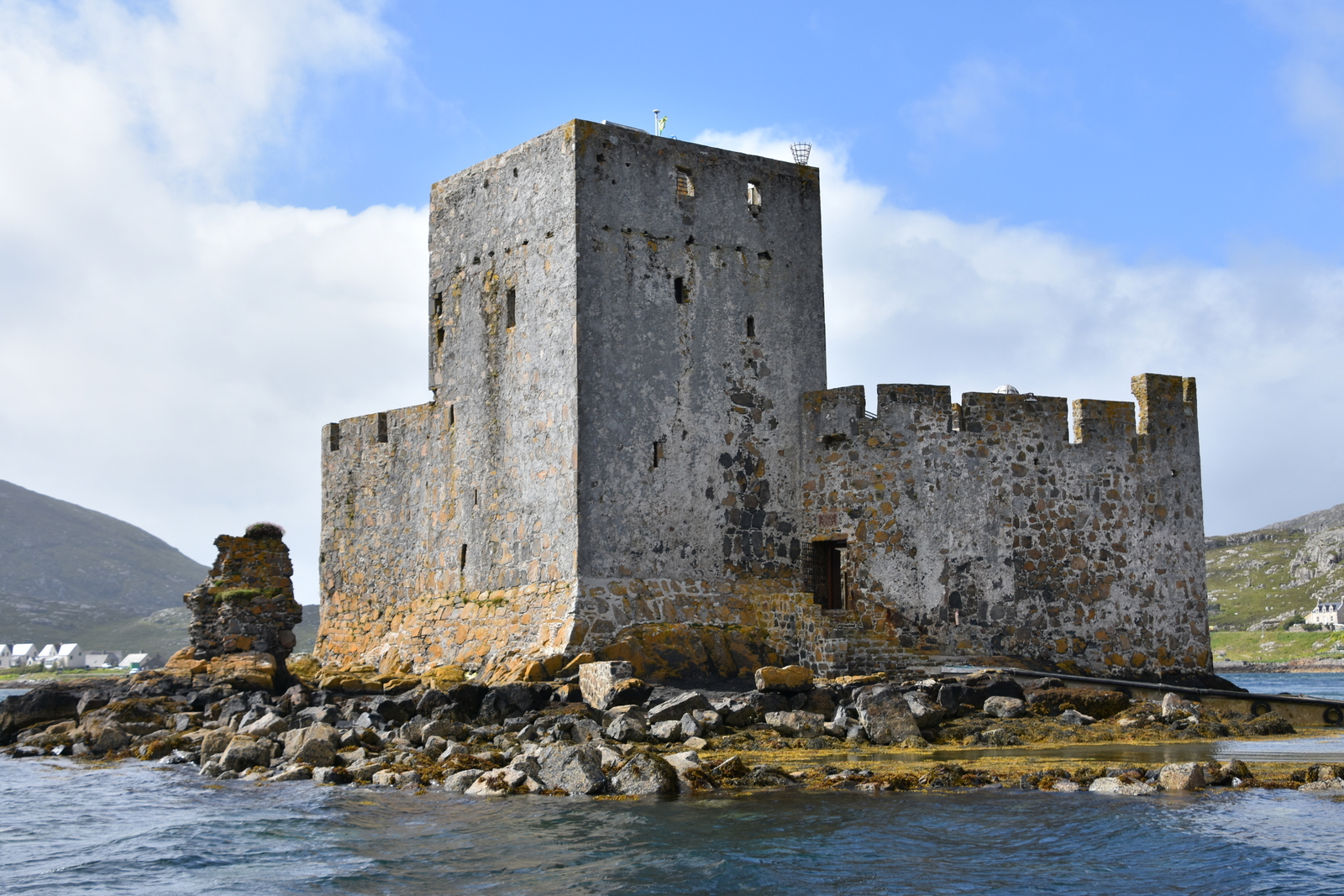 Photo of a square, grey stone-built castle with a squat square tower, on an island in a loch.