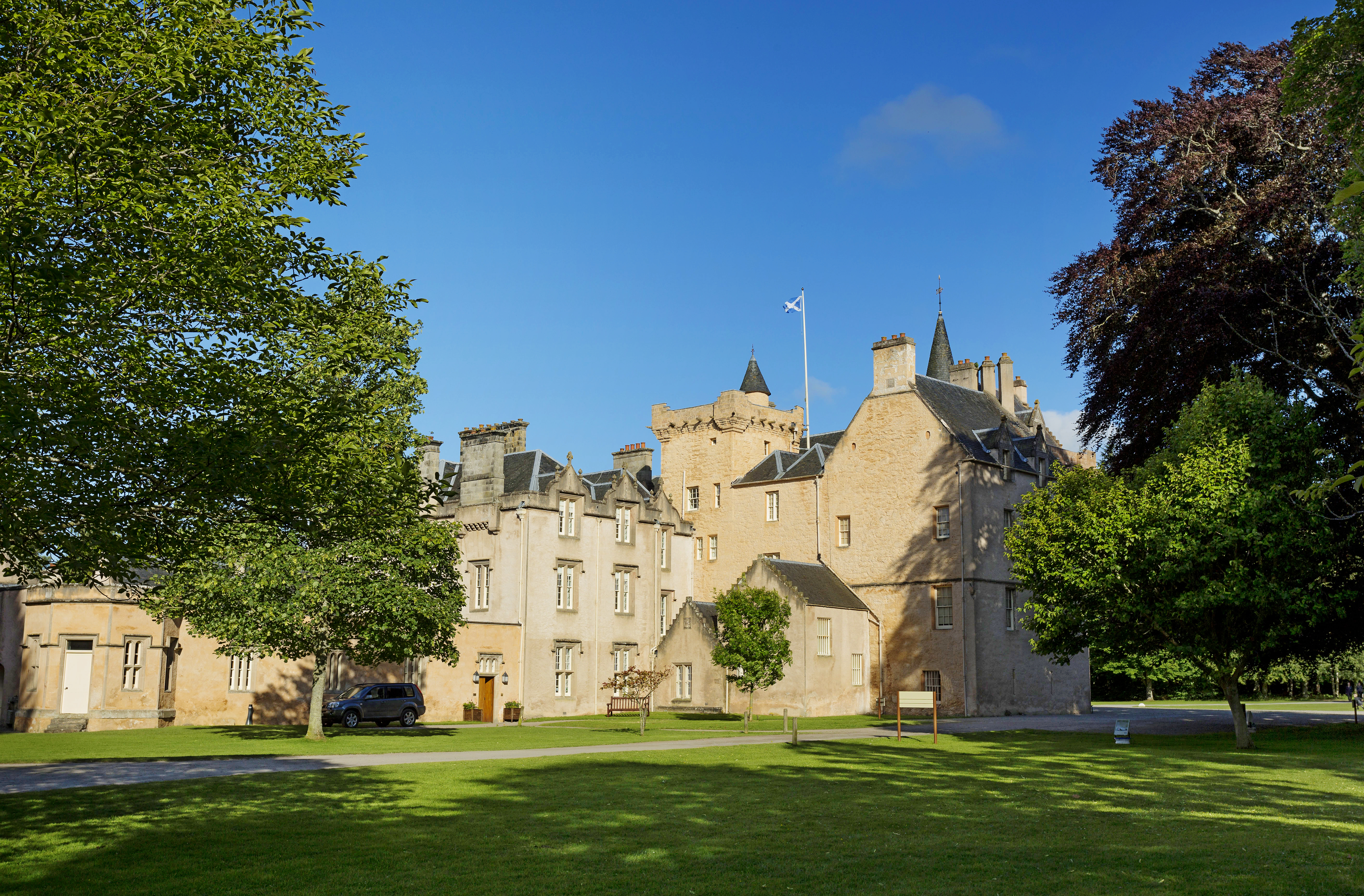 Photo of a sandstone-coloured baronial castle on a green lawn.