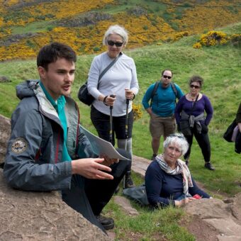 People outdoors listening to a guide on a rock