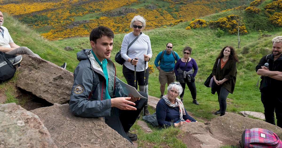People outdoors listening to a guide on a rock