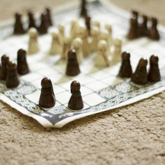 Photo of a checkered board game with small, pawn-like pieces of two different colours.