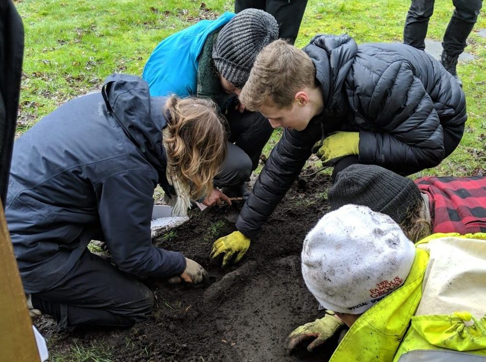 A group of people crowding around as people uncover a gravestone