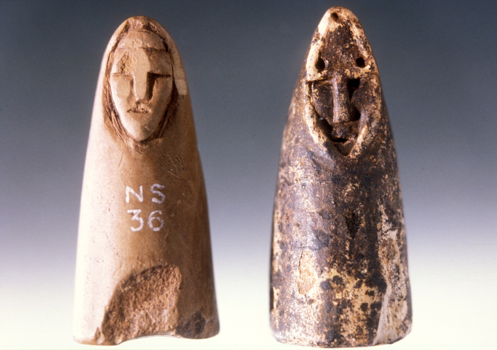 Photo of two conical gaming pieces, each shaped with a face appearing from a hood.