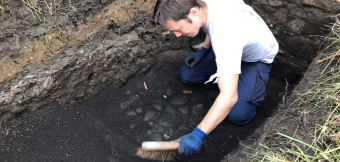 A person crouching down in a trench using a brush
