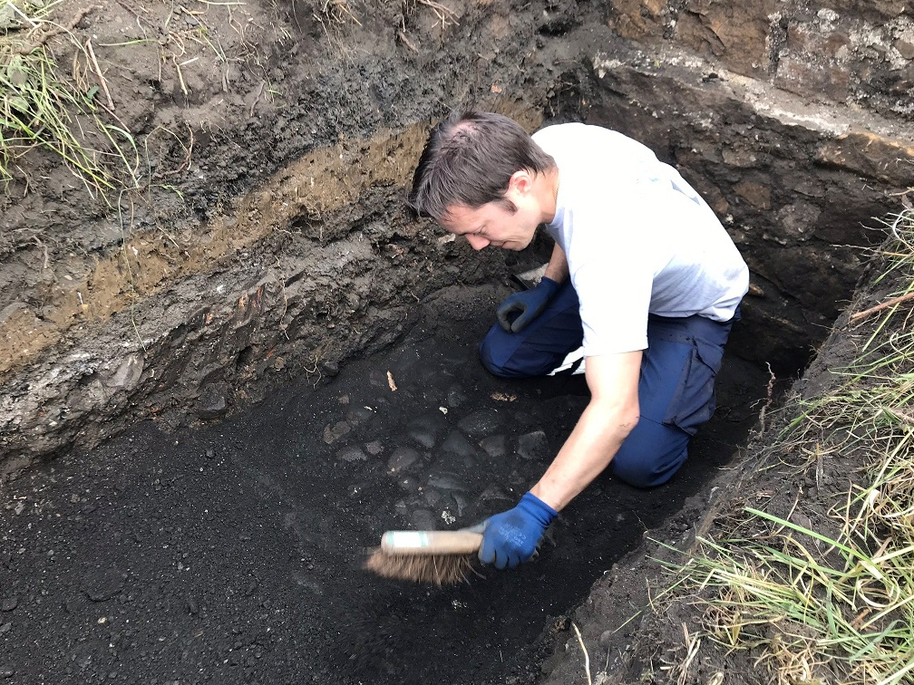 A person crouching down in a trench using a brush