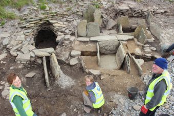 Three people standing in front of a excavated stone site