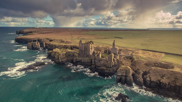 Aerial photo of the stone ruins of a large castle perched on the edge of a cliff.
