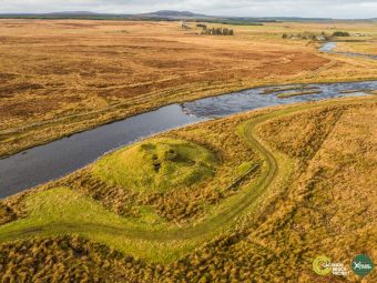 Aerial photo of the earthwork remains of a prehistoric round tower by a river.
