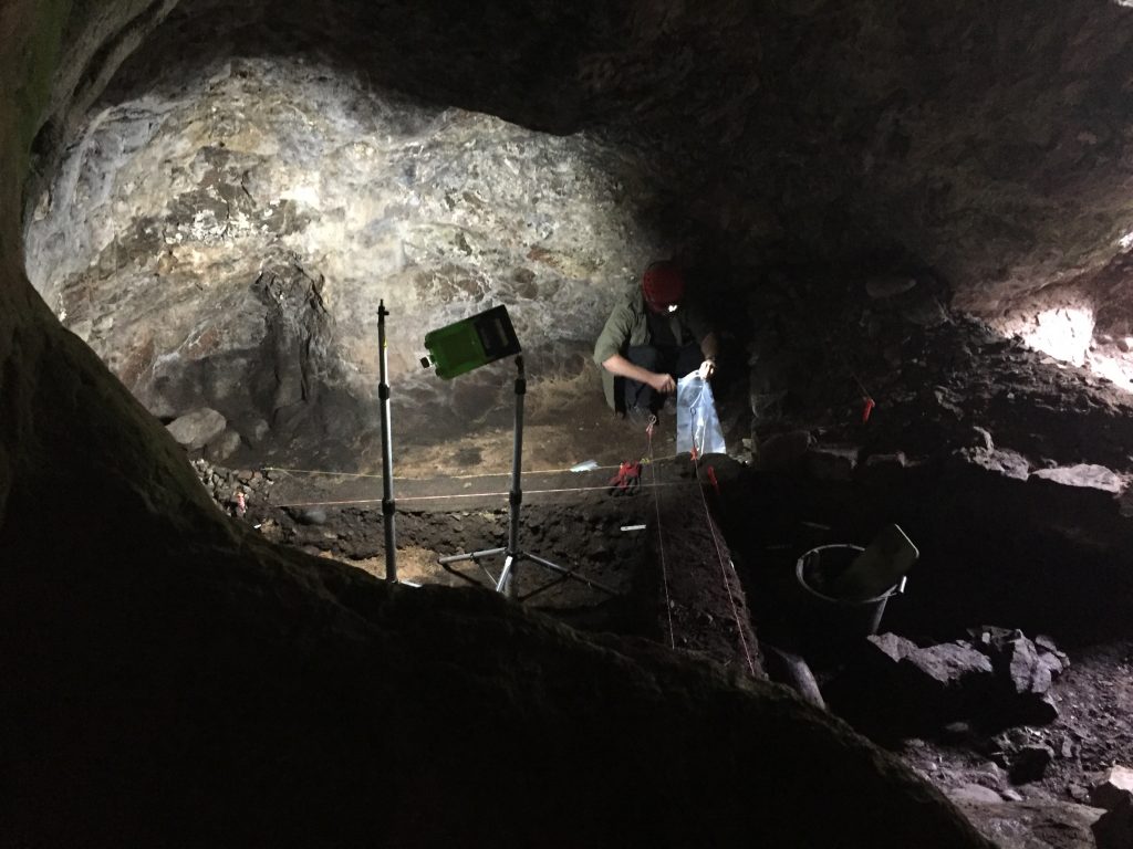 People working in a cave with a trench lit up by a light