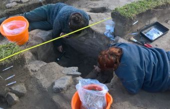 Photo of two people lying on the ground digging out a hole with trowels.