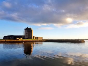 Photo of a small castle with a square central tower across a body of water.