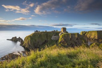 Photo of the remains of a castle on the edge of a cliff by the sea.