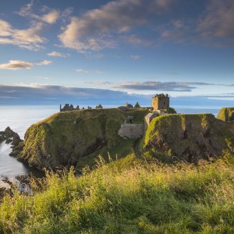 Photo of the remains of a castle on the edge of a cliff by the sea.