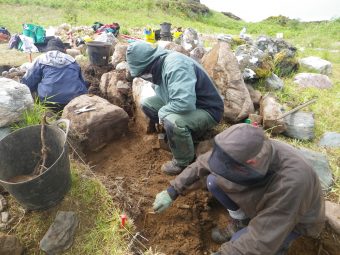 Photo of three people wearing waterproof clothing in an archaeological trench.
