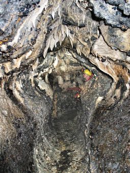 Photo of the interior of a cave passage with a person wearing a hard hat appearing at the end.