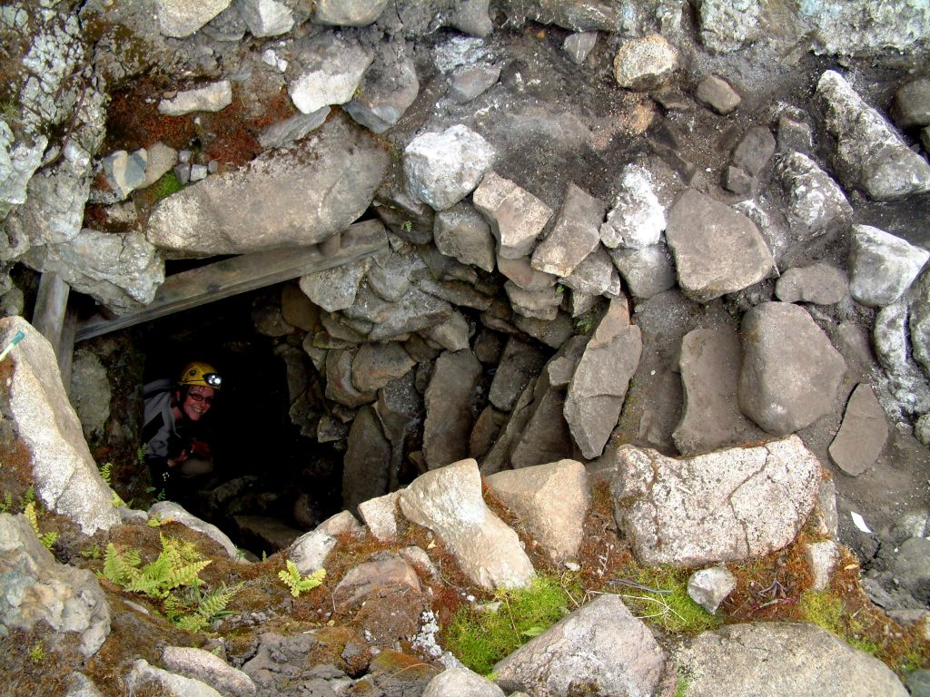 Photo of the opening to a cave system surrounded by rocks.